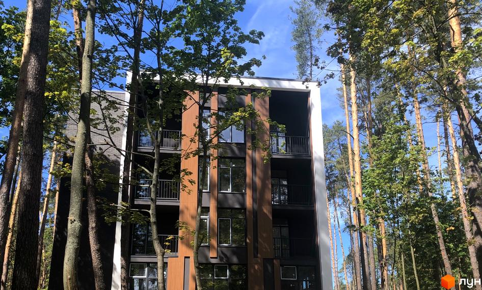 Новобудова ЖК Forest Park з дерев'яними та темними фасадами, розташована серед високих дерев. Будинок має балкони та великі вікна, що виходять на зелену зону.