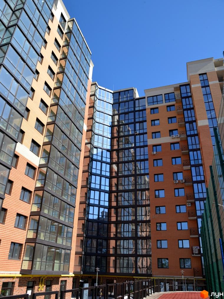 Новобудова ЖК Яровиця з цегляним фасадом та панорамним склінням. Сучасна архітектура та великі вікна, що відображають синє небо.