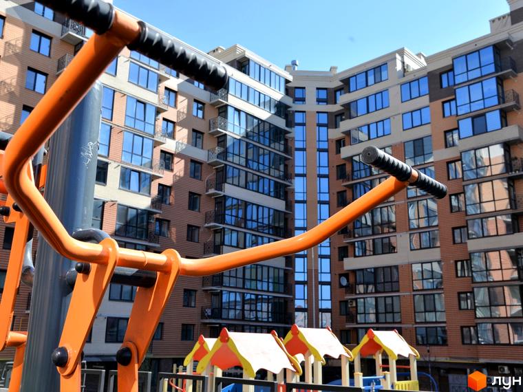 Житловий комплекс Яровиця з оранжевим спортивним майданчиком на прибудинковій території. Багатоповерхові будинки з великими вікнами та балконами.