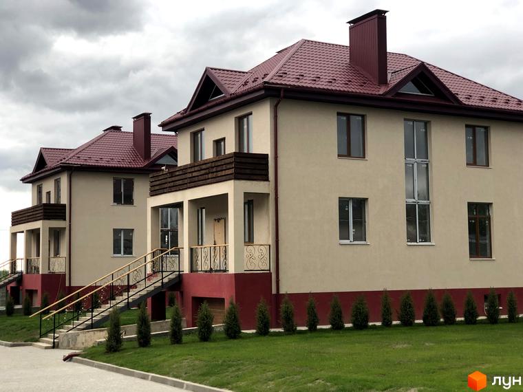 Котеджне містечко КМ Горобиновий маєток. Двоповерхові будинки з червоними дахами та світлими фасадами, огороджена територія з газоном та молодими деревами.