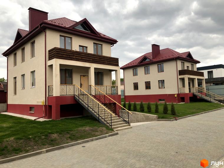 Котеджне містечко КМ Горобиновий маєток. Два двоповерхові будинки світло-бежевого кольору з червоними дахами та цоколем, розташовані на доглянутій зеленій ділянці з бруківкою.