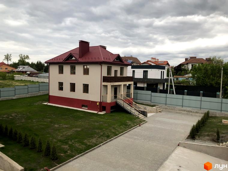 Котеджне містечко КМ Горобиновий маєток: двоповерховий будинок світло-бежевого кольору з червоним дахом, зелена галявина та вимощена бруківкою доріжка.
