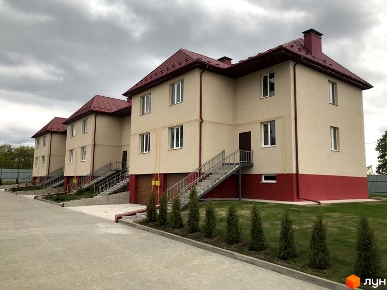 Котеджне містечко КМ Горобиновий маєток: триповерхові будинки з червоними дахами та бежевими фасадами, зовнішні сходи та доглянута прибудинкова територія з газоном та туями.