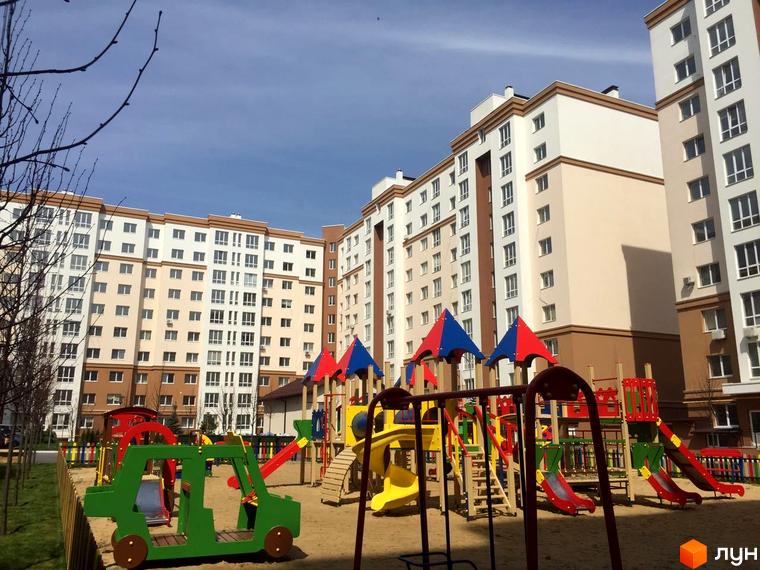 Новобудова ЖК Львівський маєток з дитячим майданчиком. Багатоповерхові будинки світло-бежевого та білого кольору з коричневими елементами.