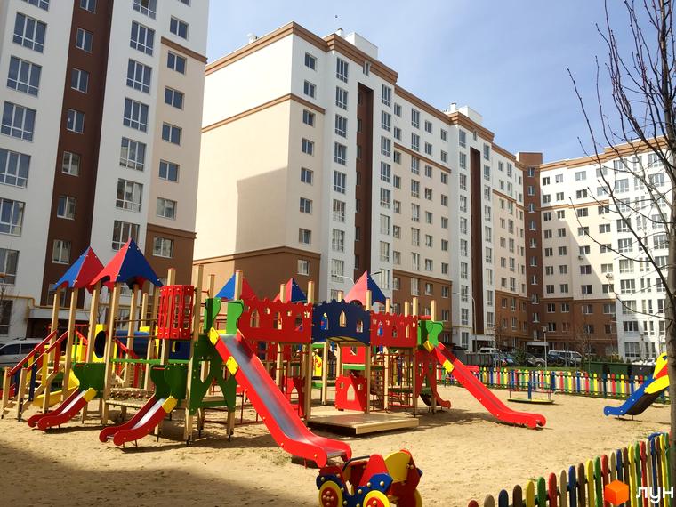 Житловий комплекс Львівський маєток з сучасним дитячим майданчиком та різнокольоровою огорожею. Багатоповерхові будинки з біло-коричневим фасадом.