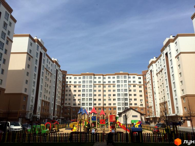 Житловий комплекс Львівський маєток: багатоповерхові будинки з бежевими та білими фасадами, дитячий майданчик з різнокольоровими елементами та огорожею.