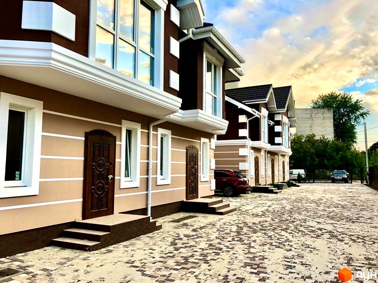 Зображення таунхаусів „КД Старокиївський“ з коричневими фасадами та великими вікнами. На передньому плані викладена бруківкою прибудинкова територія.