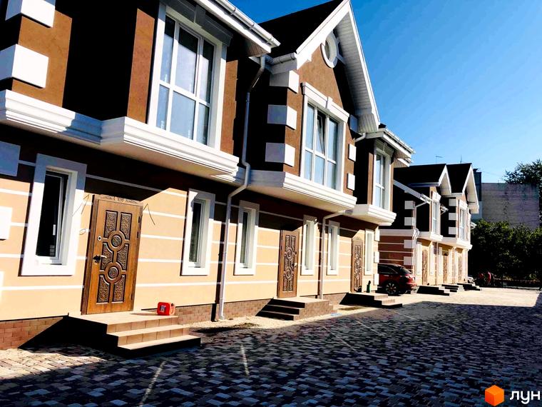 Зовнішній вигляд таунхаусів «КД Старокиївський» з коричневими стінами та білими вікнами. На передньому плані вимощена бруківкою територія.