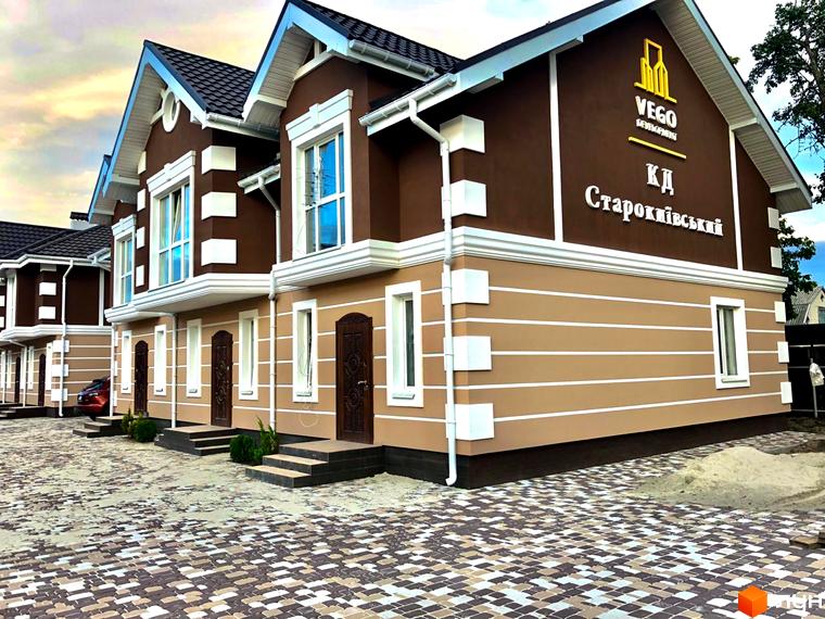 Таунхауси «КД Старокиївський» з коричневими стінами та білим декором. На подвір'ї викладена тротуарна плитка.