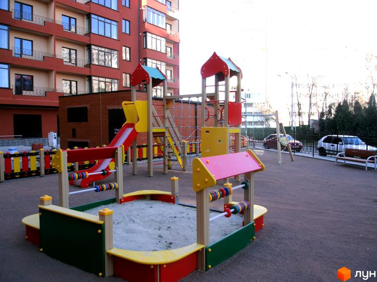 Житловий комплекс Академмістечко: багатоповерховий будинок з дитячим майданчиком. Пісочниця, гірки та інше обладнання для ігор на подвір'ї.