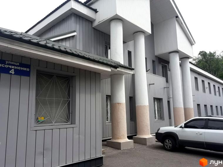 Зовнішній вигляд житлового комплексу на вулиці Михайлика, 4. Будинок має сірий фасад та колони. На прибудинковій території видно білий автомобіль.