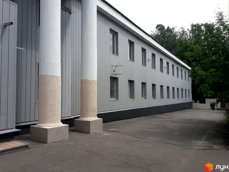 Зовнішній вигляд будівлі з колонами та сірим фасадом на вулиці Михайлика, 4. Навколо будівлі асфальтована прибудинкова територія та зелені дерева.