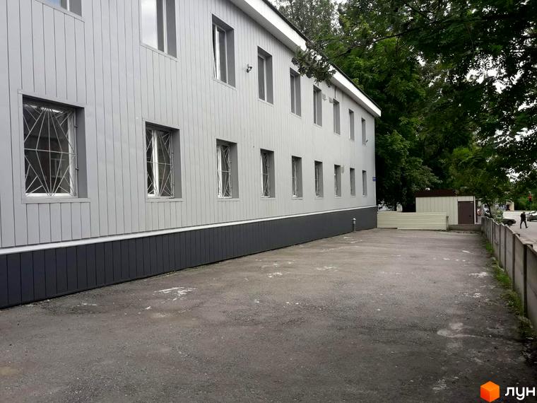 Зовнішній вигляд будівлі з сірим фасадом та вікнами з решітками на вулиці Михайлика, 4. Прибудинкова територія з асфальтованим покриттям та огорожею.