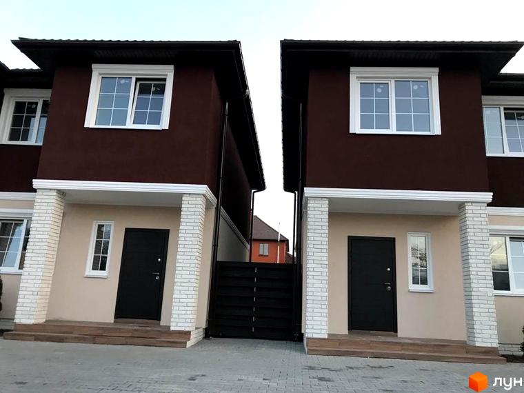 Двоповерхові будинки з коричневими стінами та білими вікнами. Перед будинками бруківка, на задньому плані видно паркан.