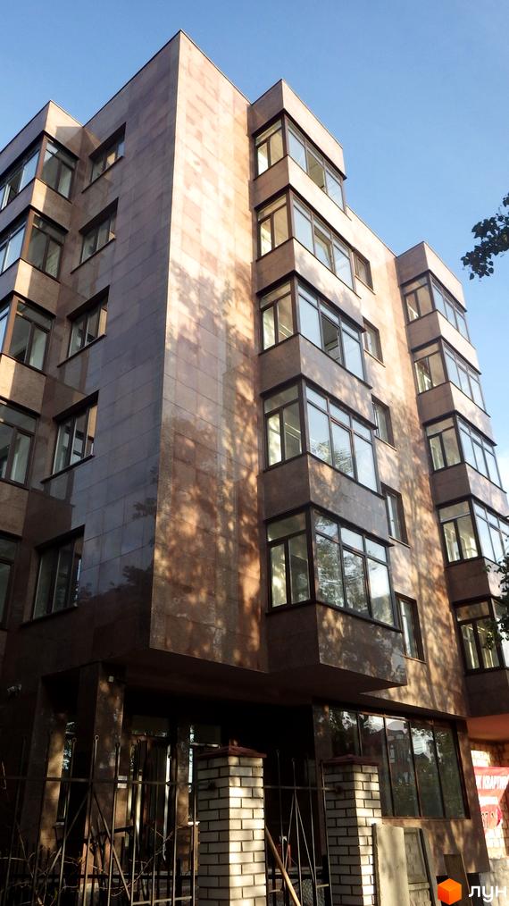 Висотна будівля з великими вікнами та облицюванням з коричневого каменю. На першому поверсі видно скляні двері та ковані огорожі.