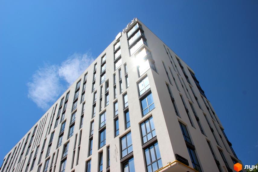 Фасад новобудови ЖК OBRIY під блакитним небом з хмарами. Будинок має багато вікон та сучасний дизайн.