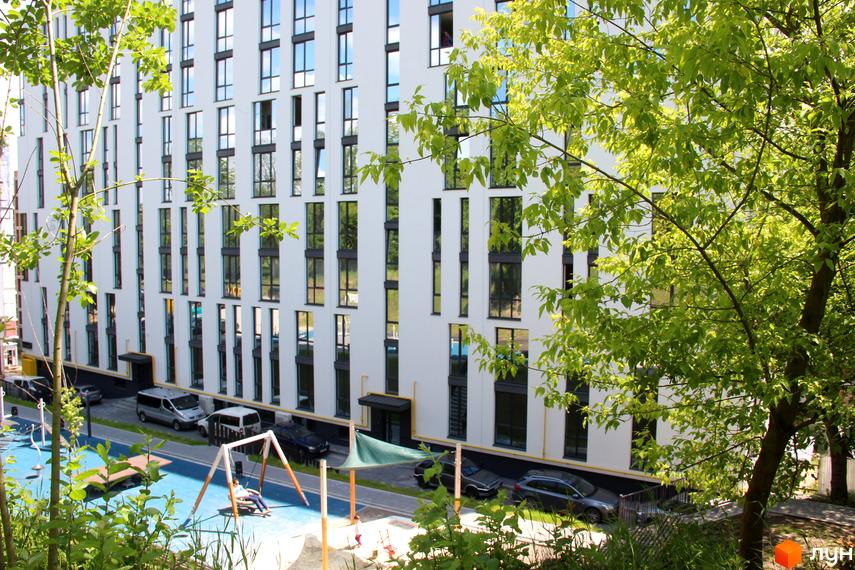 Новобудова ЖК OBRIY з білим фасадом та великими вікнами. На прибудинковій території дитячий майданчик та місця для паркування.