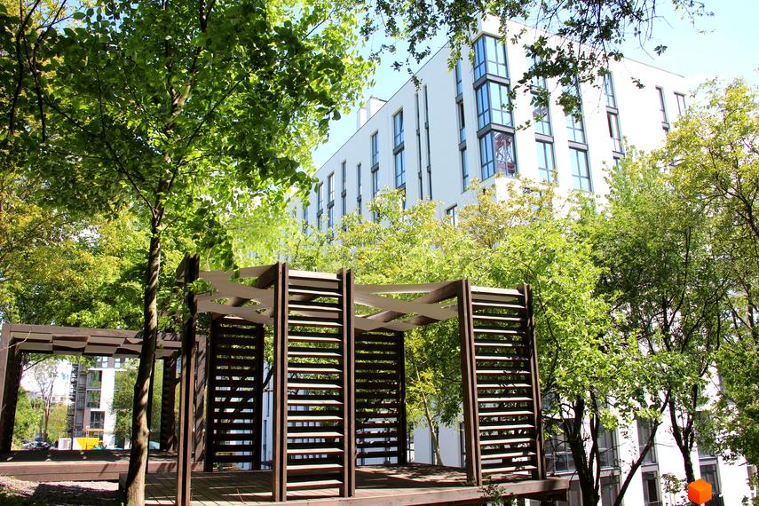 Новобудова ЖК OBRIY з білим фасадом та великими вікнами, оточена зеленню та дерев'яною альтанкою.