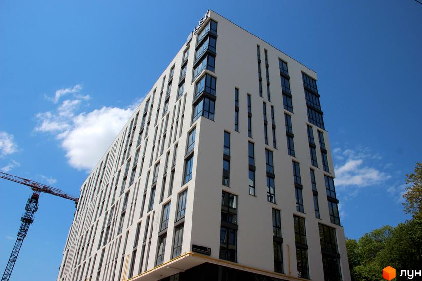 Фасад новобудови ЖК OBRIY з численними вікнами та виступаючими елементами. Поруч видно будівельний кран на фоні блакитного неба з хмарами.