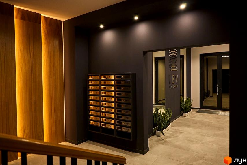 Сучасний вхід в ЖК OBRIY з дерев'яними панелями та підсвіткою. У вестибюлі розташовані поштові скриньки та рослини.