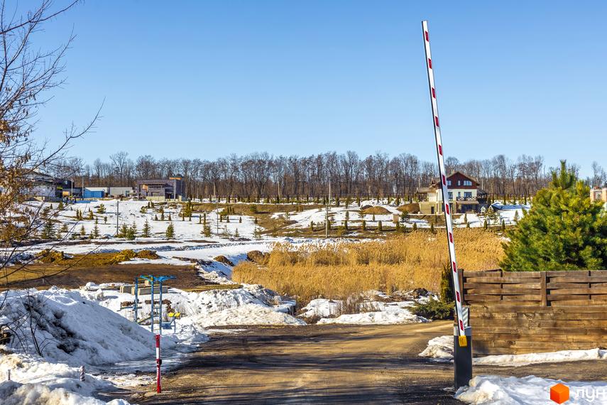 Котеджне містечко Шалє Грааль. Двоповерховий будинок з дерев'яним парканом та шлагбаумом на в'їзді. Навколо сніг та дерева.