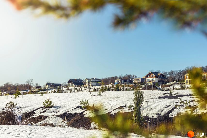 Будинки в котеджному містечку Шале Грааль з великими вікнами та світлими фасадами, розташовані на засніженій території з молодими деревами.