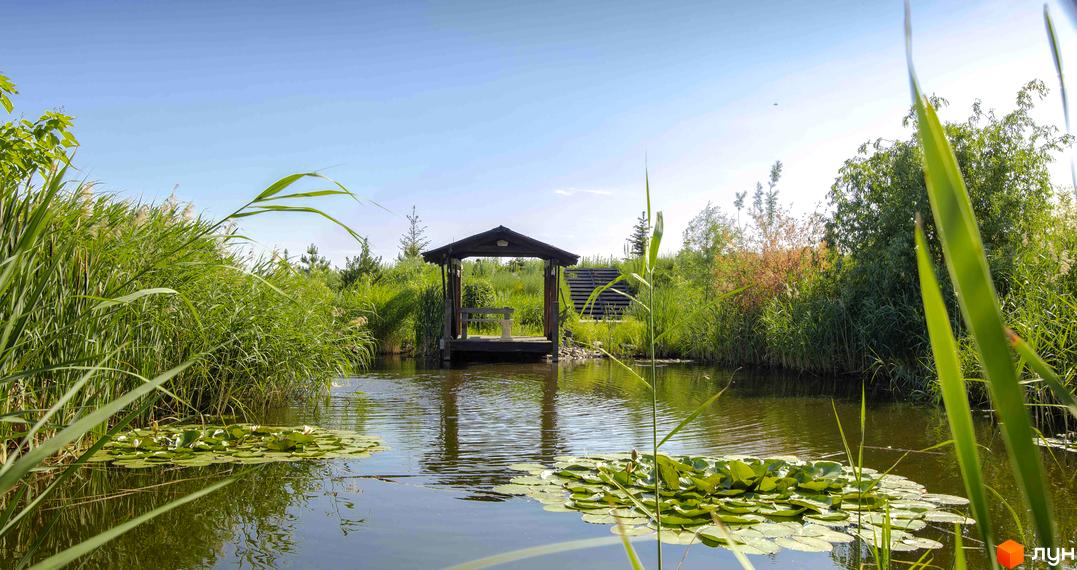 Котеджне містечко Шалє Грааль: дерев'яна альтанка на березі озера з лататтям та очеретом, зелена територія.