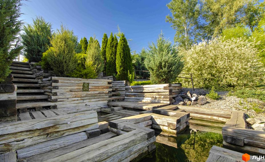 Котеджне містечко Шалє Грааль. Дерев'яні тераси та сходинки біля водойми, зелені насадження навколо будівель.