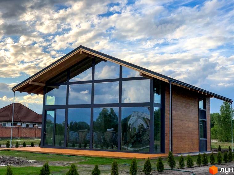 Котеджне містечко Riviera Sunrise з панорамними вікнами та дерев'яною обшивкою фасаду, розташоване на фоні хмарного неба та зеленої прибудинкової території.