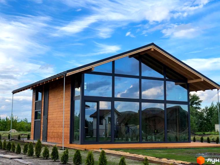 Котеджне містечко КМ Riviera Sunrise з дерев'яними стінами та панорамними вікнами, навколо зелені насадження та доглянута територія.