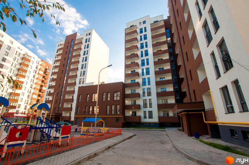 Житловий комплекс Еко-дім на Мечникова 2. Зовнішній вигляд будівель з коричневими та білими фасадами, балконами та вікнами. Прибудинкова територія з дитячим майданчиком та бруківкою.