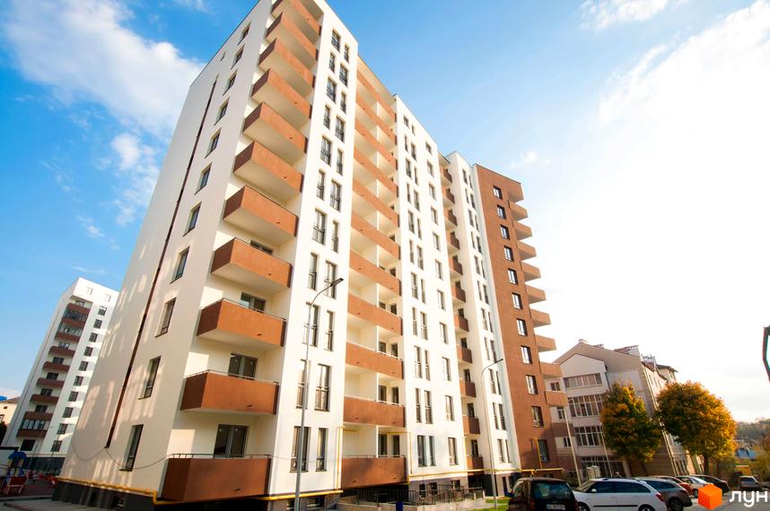 Новобудова Еко-дім на Мечникова 2 з біло-коричневим фасадом та численними балконами. Навколо будівлі розташовані припарковані автомобілі та дерева.