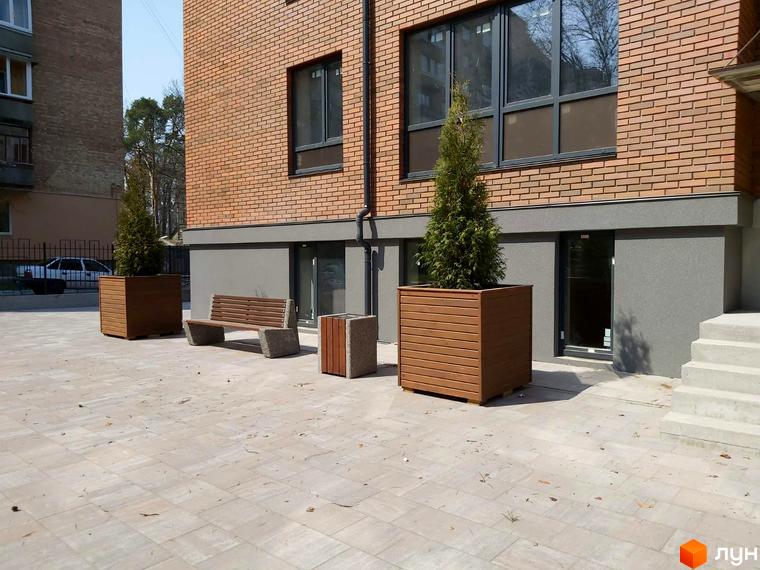 Житловий комплекс Brighton Residence з цегляним фасадом та зеленими насадженнями на прибудинковій території. Наявні лавки та великі клумби.