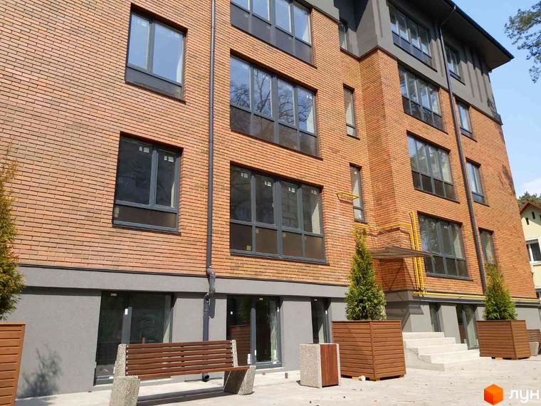 Будинок ЖК Brighton Residence з цегляним фасадом та великими вікнами. Поруч розташовані зелені насадження та лава для відпочинку.