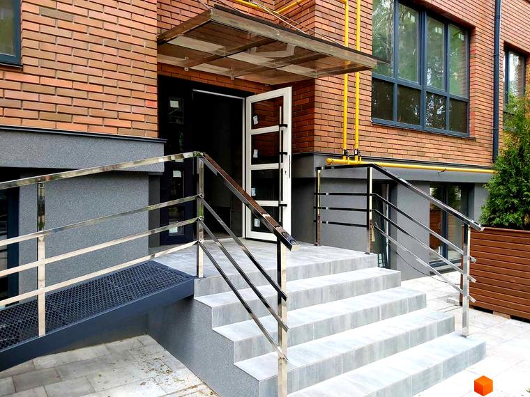 Вхідна група житлового комплексу Brighton Residence з пандусом та сходами, оздобленими цеглою та металевими поручнями.