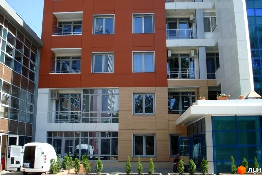 Фасад житлового комплексу Сігурд Холл з великими вікнами та балконами. Прибудинкова територія з зеленими насадженнями та паркувальними місцями.