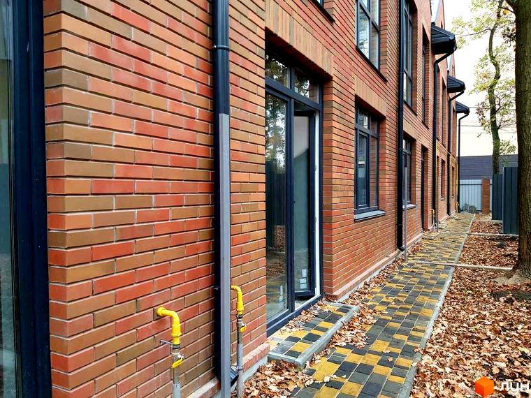 Таунхауси Brighton-park: цегляний фасад будівлі з вікнами та доріжкою з бруківки з опалим листям.