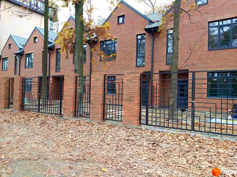 Таунхауси Brighton-park з червоної цегли з чорними вікнами та огорожею. Навколо будівель опадає осіннє листя.