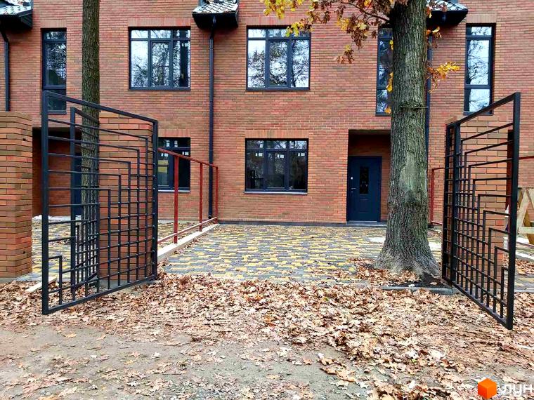 Цегляний будинок з темними вікнами та вхідними дверима. Перед будинком розташовані ковані ворота та осіннє листя.