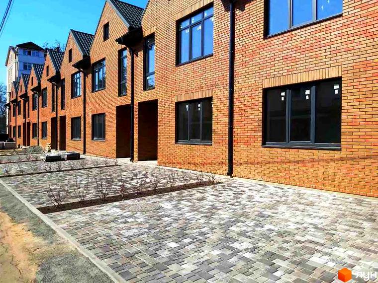 Зовнішній вигляд таунхаусів Brighton 3 з цегляними фасадами та брукованою прибудинковою територією. Видно вікна та чорні водостічні труби.