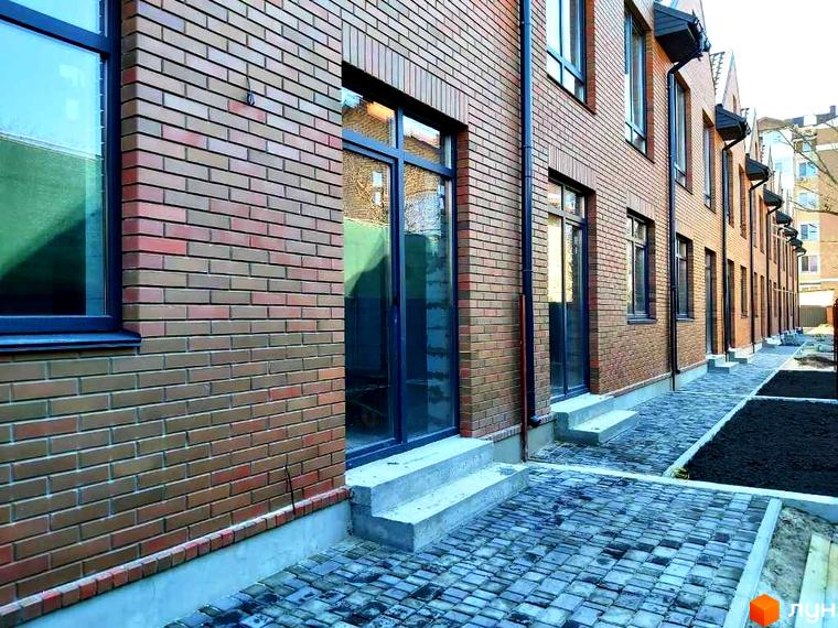 Цегляний будинок з великими вікнами та скляними дверима. Бруківка на тротуарі та клумби з чорним ґрунтом створюють затишну атмосферу.