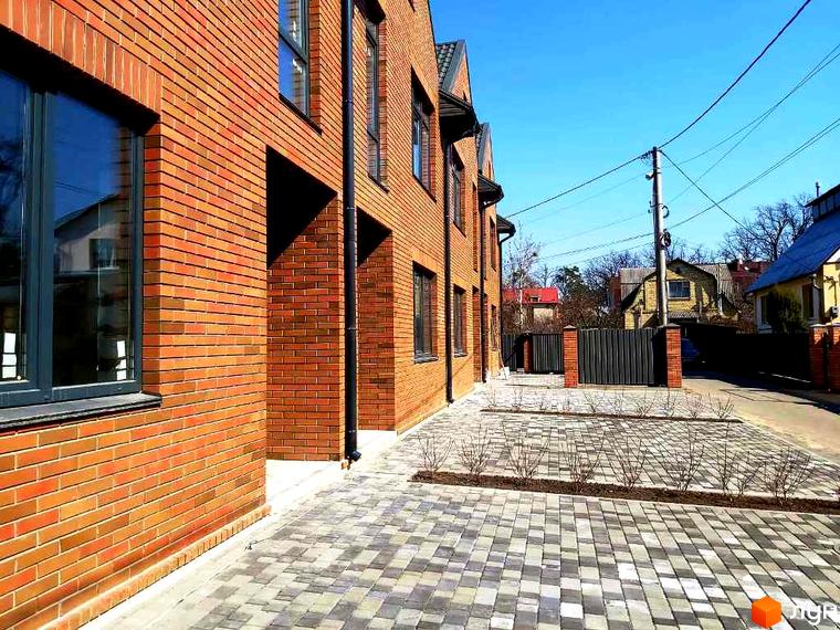 Зовнішній вигляд таунхаусів „Brighton 3“ з червоної цегли. Бруківка на прибудинковій території та зелені насадження.