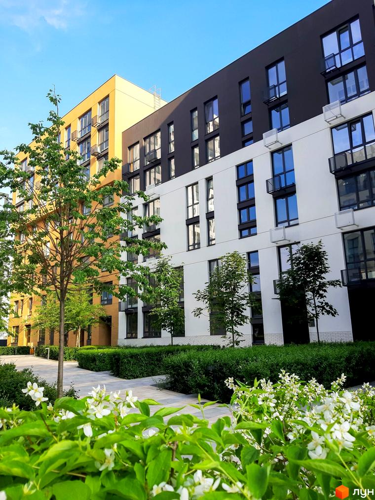 Житловий комплекс Файна Таун з яскравим фасадом. На передньому плані квіти та зелені насадження, що створюють затишну атмосферу.