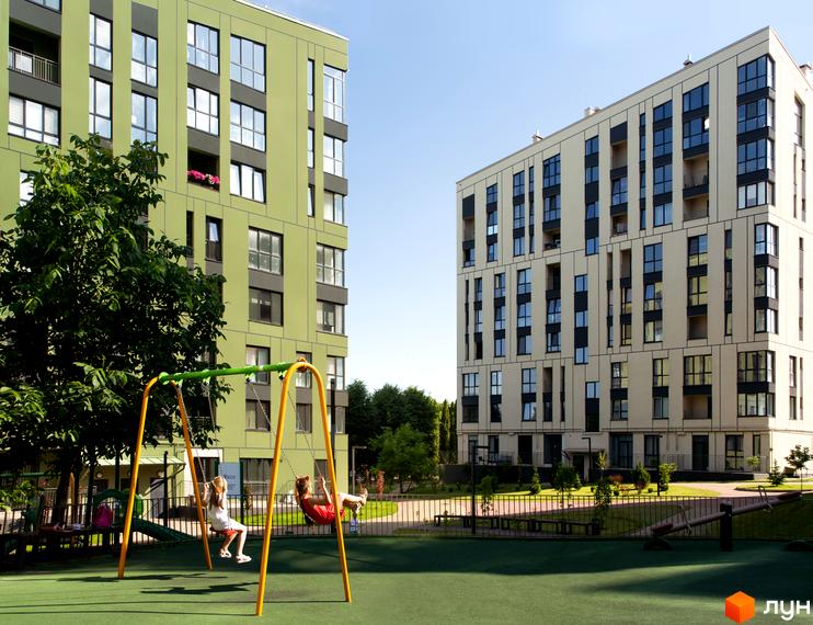 Житловий комплекс Spectrum. Два багатоповерхові будинки, один світло-бежевий, інший зелений. На прибудинковій території дитячий майданчик з гойдалками та дітьми.