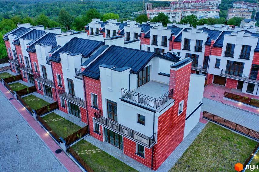 Таунхауси Raytman Park з червоно-білими фасадами, темними дахами та балконами. Прибудинкова територія має зелені газони та вимощені доріжки.