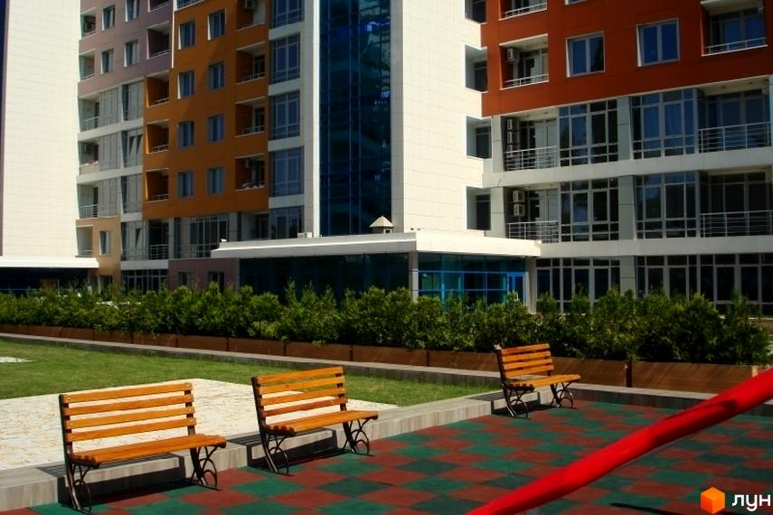 Зовнішній вигляд житлового комплексу ЖК Сігурд Холл з панорамними вікнами та прибудинковою територією з лавками та зеленими насадженнями.