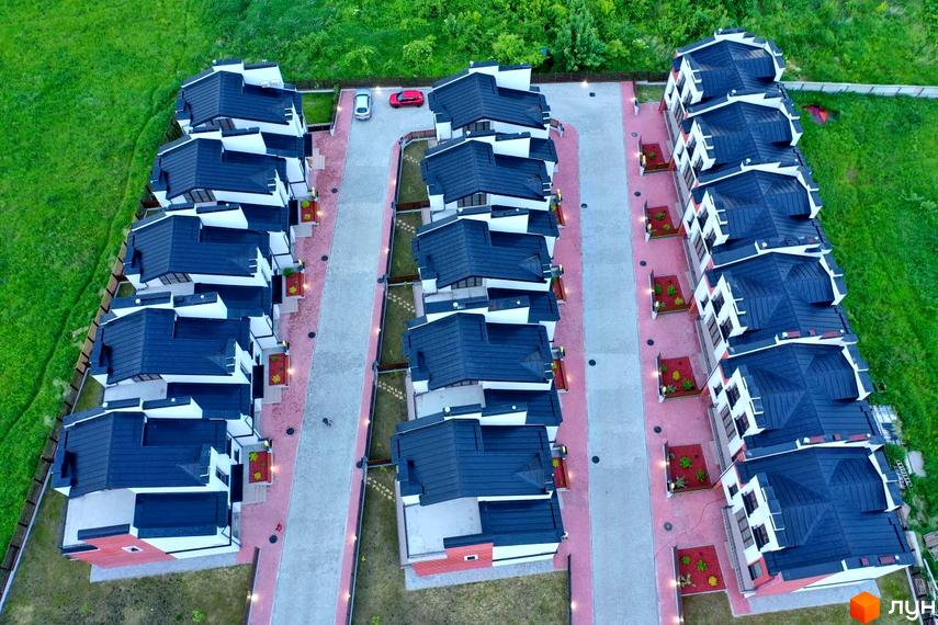 Ряд таунхаусів Raytman Park з темними дахами та світлими фасадами. Видно доріжки, зелені газони та освітлення території.