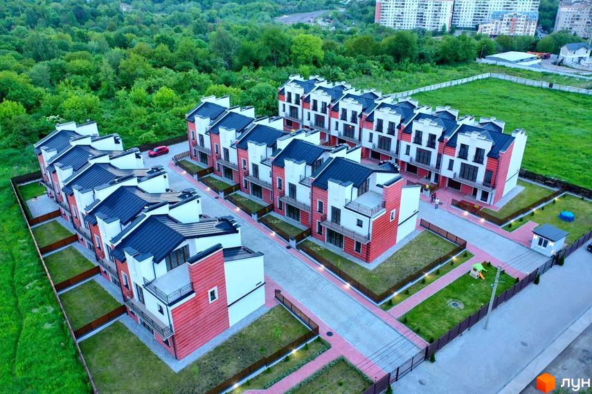 Таунхауси Raytman Park з червоно-білими фасадами, темними дахами та балконами. Прибудинкова територія облаштована газонами, брукованими доріжками та дитячим майданчиком.