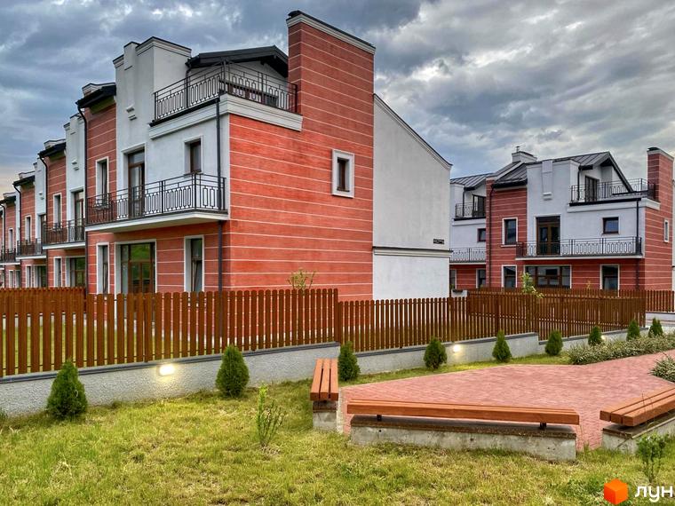 Таунхауси Raytman Park з червоно-білими фасадами та чорними балконами. Прибудинкова територія має зелений газон, дерев'яний паркан та лавки.