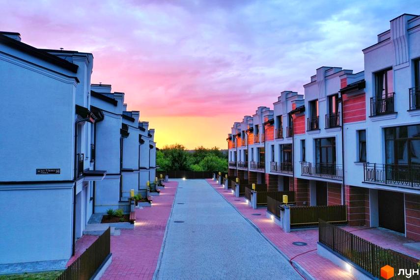 Таунхауси в Житловому комплексі Raytman Park з білими стінами та балконами. Вид на вулицю з тротуарною плиткою та зелені насадження.